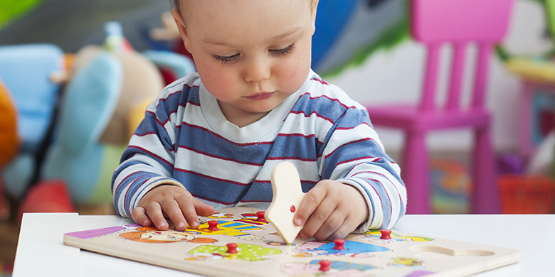 Toddler or a baby child playing with puzzle in a nursery.
