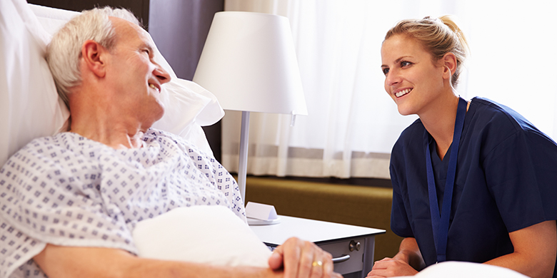 Patient Care Technician Talking To Senior Male Patient In Hospital Bed