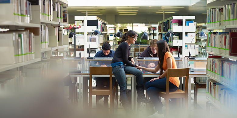 group of college students studying in library, two girls talking together.