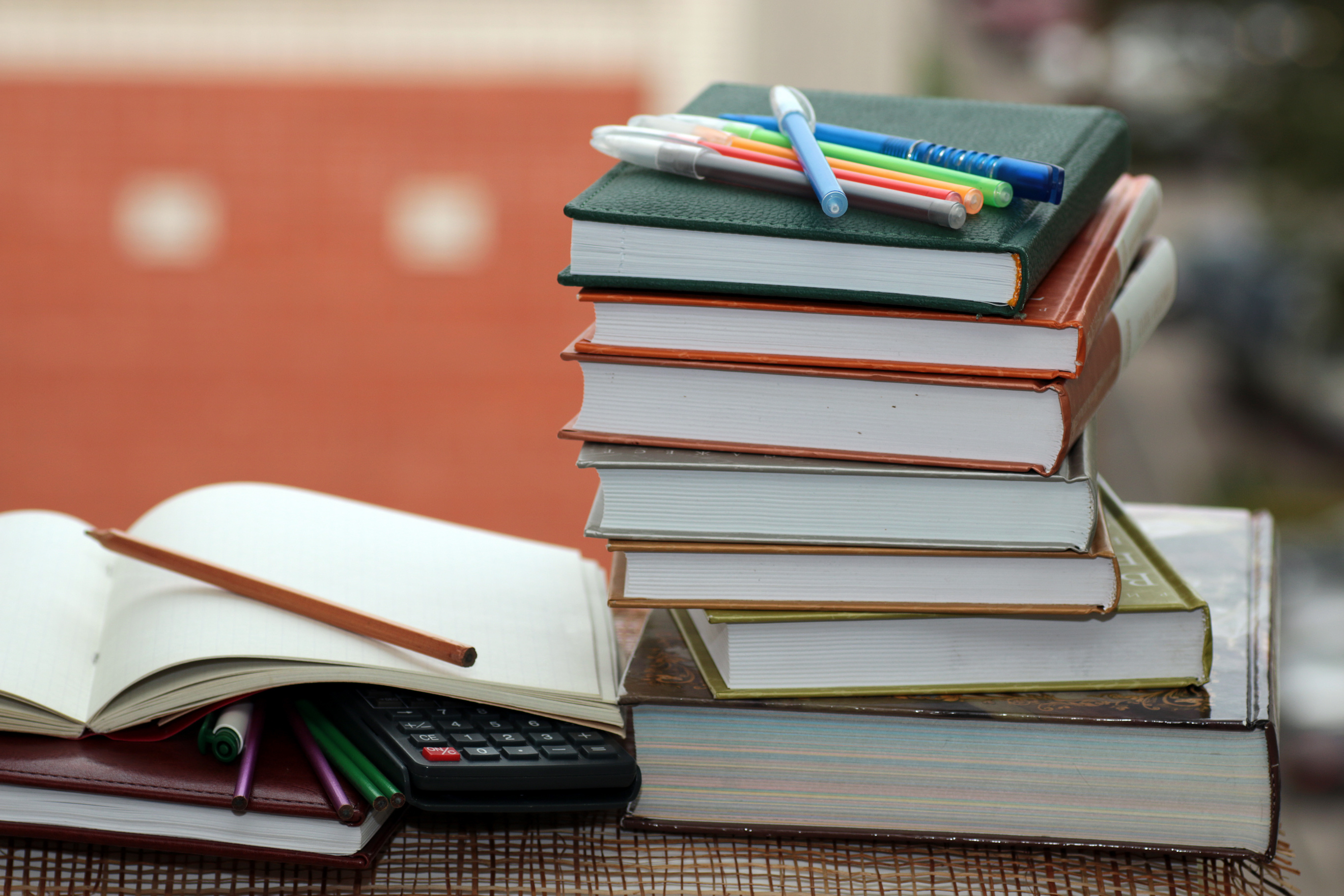 Several books stacked up with pens layed on top of stack. One book open with pencil laying across the page.