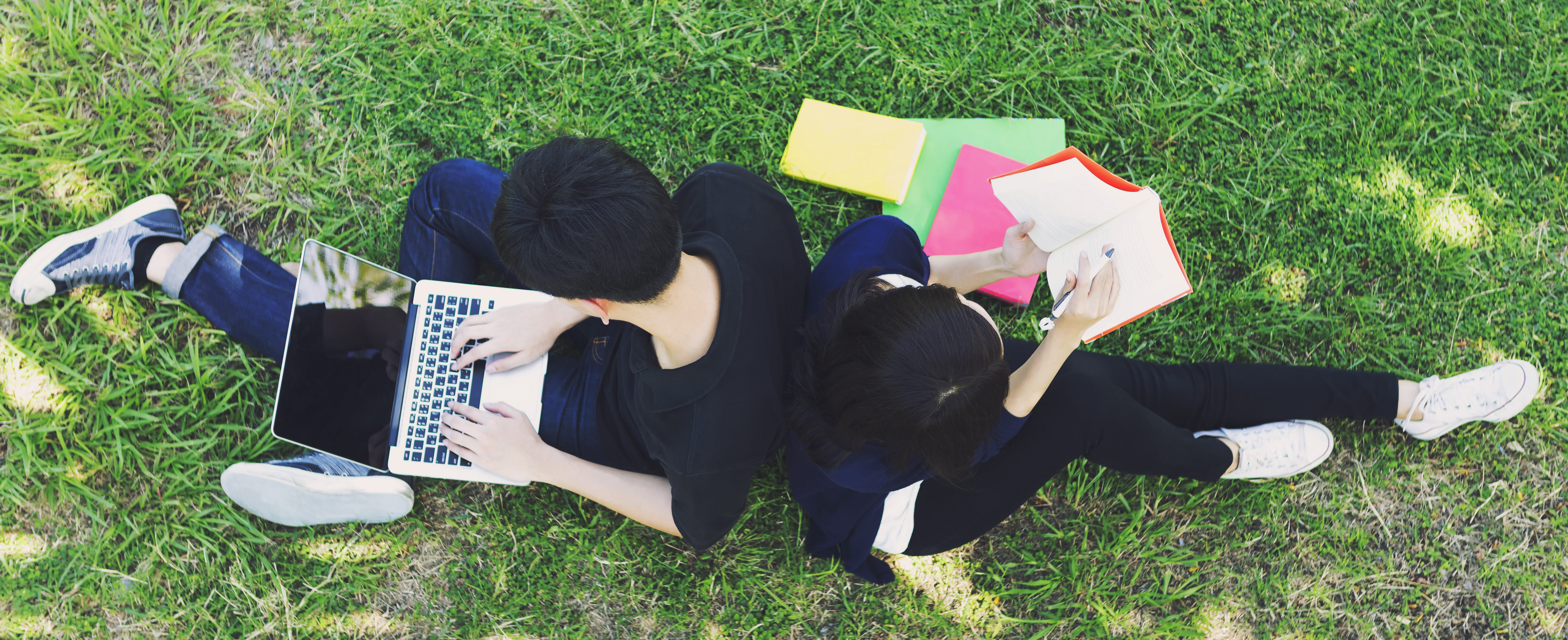 Young students siting on green grass and reading in top view. Education concept.